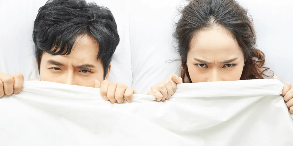 布団の中で怒る女性と反省する男性